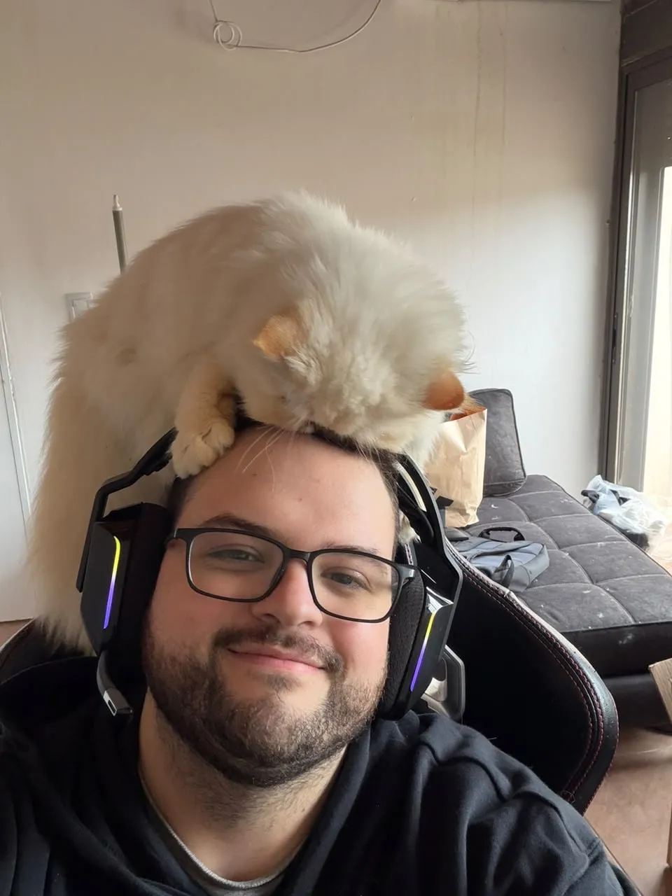 Mayco Faciolo wearing a headset, with a fluffy white cat sitting on their head